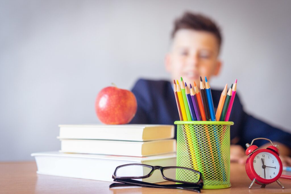 Pencils in cup holder and miscellaneous items with student blurred in background