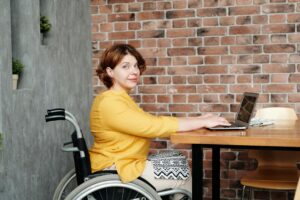 Woman in wheelchair working at desk on laptop.